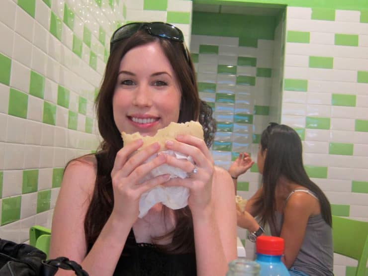 Tori Avey eating a falafel pita sandwich, smiling at the camera, at Mana Mana restaurant in Tel Aviv, Israel.