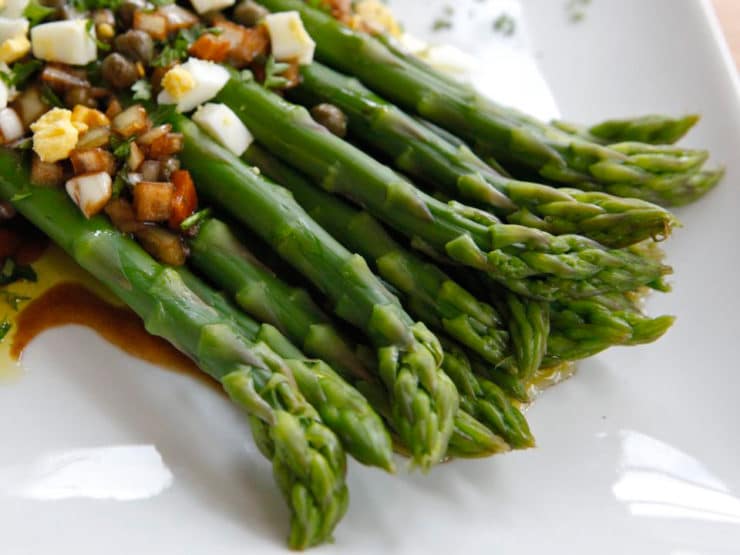 A close up shot of Marinated Asparagus with hard cooked egg, capers, and herbs served on a white plate.