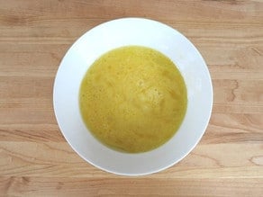 Egg and oil mixed together in a white ceramic bowl on a wooden cutting board background.