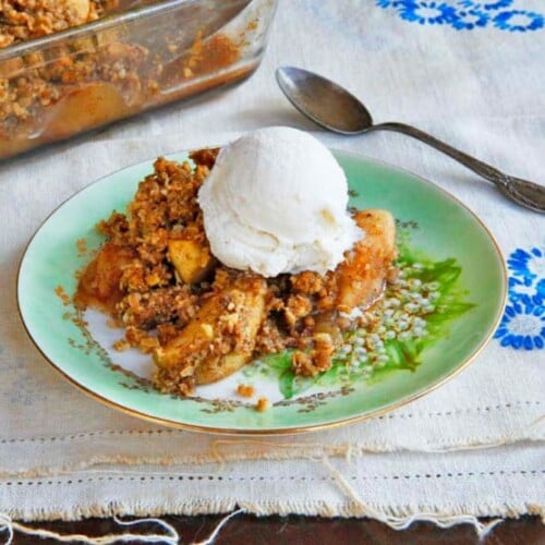 A delicious Oat Nut Apple Crisp dessert with a golden brown crumble and ice-cream topping served in a white ceramic dish