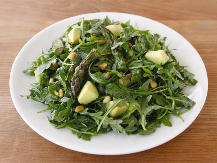 A white plate full of Roasted Asparagus, Avocado and Arugula Salad on topped of a table