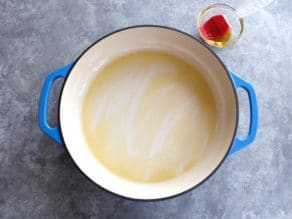 Enameled casserole dish brushed with olive oil, red silicone brush in bowl on the side, grey concrete background.