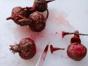 Chef's knife slicing tops and tips from roasted beets on a white cutting board.