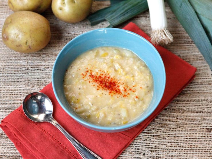 Smoky Potato Leek Soup topped with paprika powder and served on a blue bowl with spoon on the left side and on top of a red table cloth