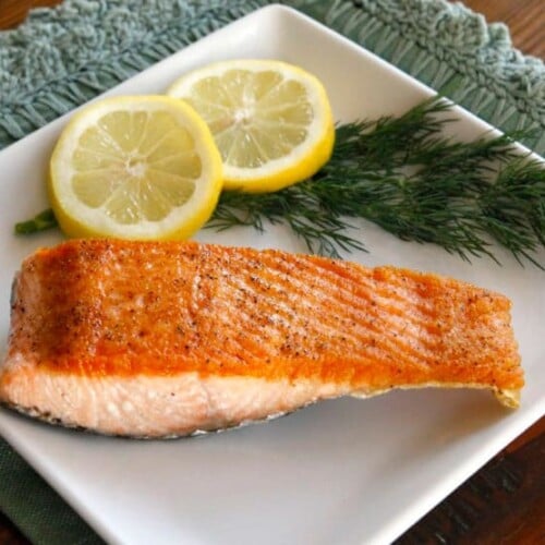 A seared salmon fillet on a white plate with lemon slices