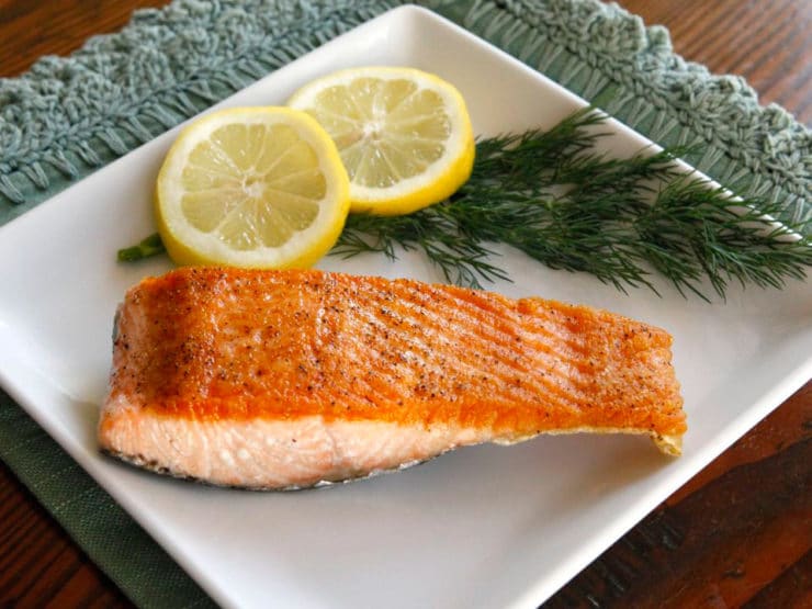 A seared salmon fillet on a white plate with lemon slices