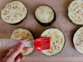 Brushing eggplant rounds with egg whites.