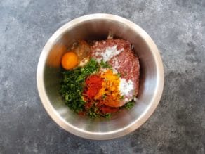 Ingredients for Middle Eastern Burgers in a stainless steel bowl on a grey concrete background.