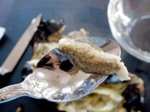 Clump of eggplant seeds in spoon scooped from roasted eggplant, roasted eggplant on cutting board in background with knife.