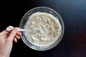 Glass bowl of roasted eggplant dip, hand stirring with fork.