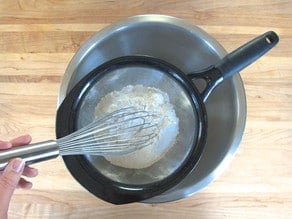 Sifting flour and other dry ingredients into a mixing bowl.