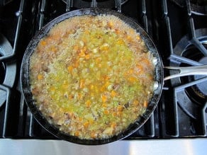 Mushroom broth added to vegetables in skillet.