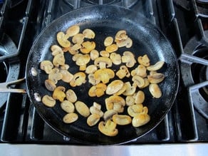 Sliced mushrooms browning in a skillet.