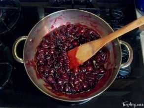 Cooked cherries on top of stove with a wooden spatula