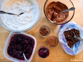 A bowl of cream, melted chocolate, cherry jam, and crushed chocolate crackers arrange neatly on a table