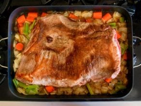 Browned brisket on top of onions, carrots and celery chopped in roasting pan on stovetop.