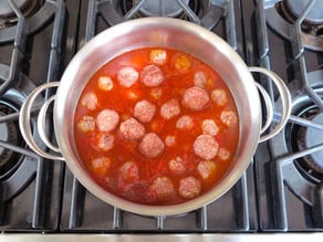 Meatballs set in stockpot of sauce.