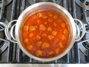 Meatballs set in stockpot of sauce.