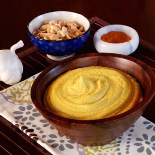 Peanut Hummus served in a brown bowl with a bowl of peanuts and spies at the back.