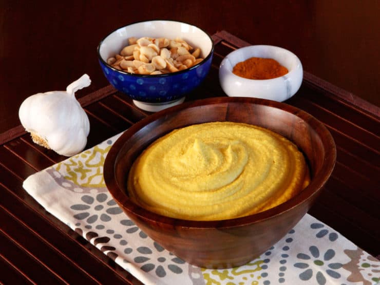 Peanut Hummus served in a brown bowl with a bowl of peanuts and spies at the back.