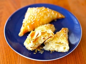 Image of two Flaky pastry filled with a savory blend of potatoes and cheese served on a blue plate with one split into half