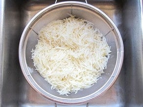 Shredded potatoes draining in a colander.