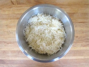 Combining shredded potatoes and onions with a fork.