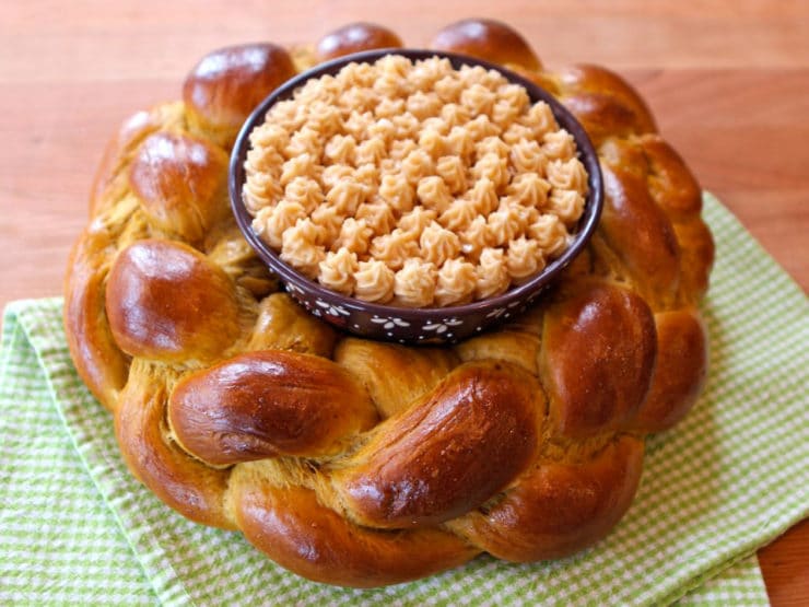 Horizontal close-up of a pumpkin challah centerpiece with honey butter, resting on a green checkered table napkin.