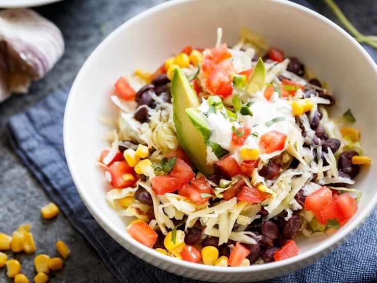 Overhead shot of Quinoa Black Bean Burrito Bowl with avocado, shredded cheese and tomatoes.