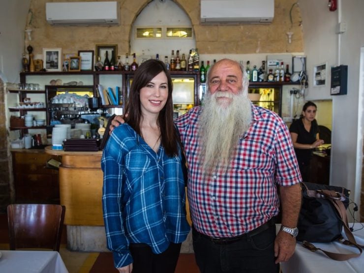 Photograph of a man with a long white beard and a brunette woman. They are Tori Avey and Chef Uri Jeremias.