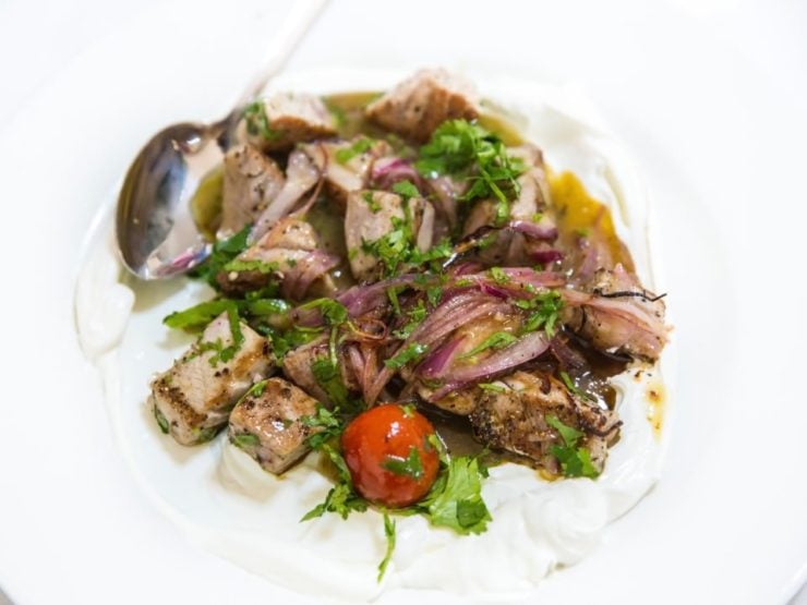 A plate of fish pieces topped with red onion, chopped green herbs, and cherry tomatoes on a white tablecloth. 