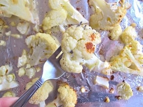 Caramelized roasted cauliflower floret pierced by fork over baking sheet.