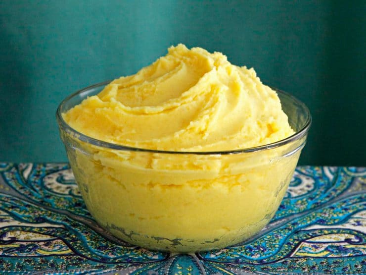 A bowl of saffron mashed potatoes, with a vibrant yellow butter, placed on a table