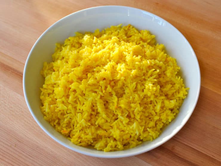 Horizontal close up shot of Saffron rice in a white bowl on top of a wood table.