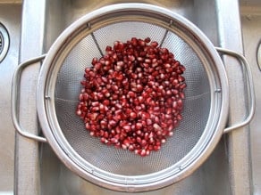 Pomegranate seeds draining in a strainer.