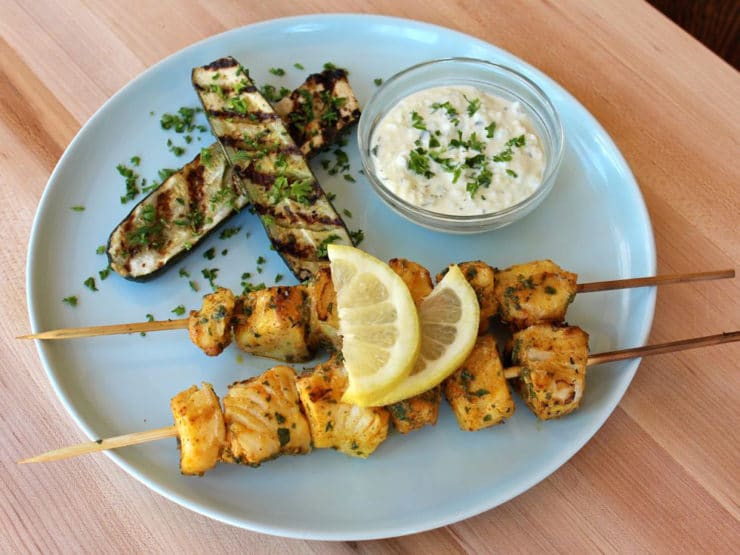 Grilled fish skewers with Mediterranean flavors on a plate with grilled eggplants and lemons