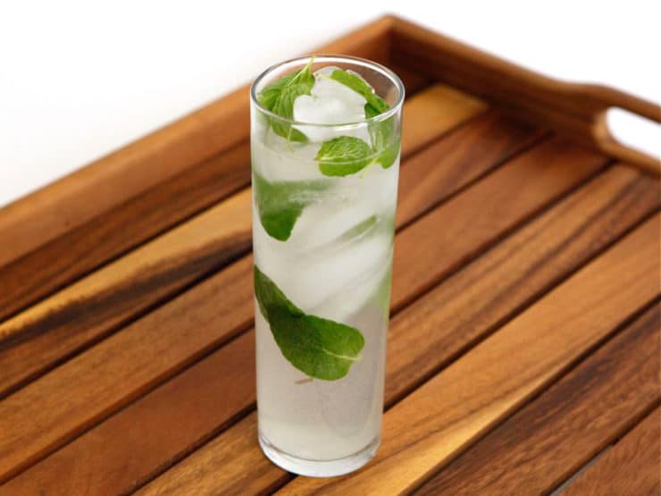 A tall glass of Mojito cocktail with mint leaves served on a wooden tray