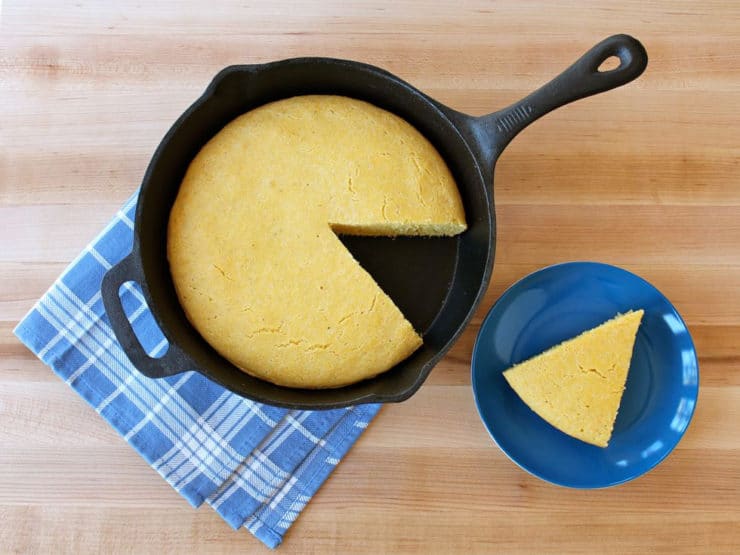 A Buttermilk Skillet Cornbread inside a pan and a single sliced Buttermilk Skillet Cornbread served on a blue plate