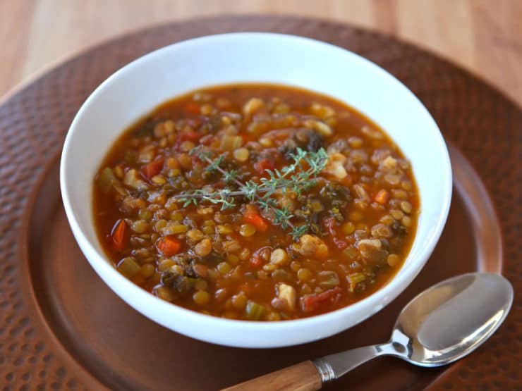 A close-up of cauliflower stew served in a white bowl, with a spoon resting beside it, all placed on a round brown tray for a rustic touch.