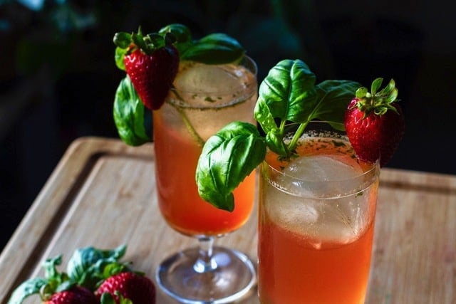 Two cocktail glasses filled with a red beverage and garnished with a sprig of basil and a strawberry.