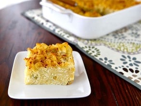 Sweet Lokshen Kugel on white plate, with container in background, on patterned placemat, on wooden table.