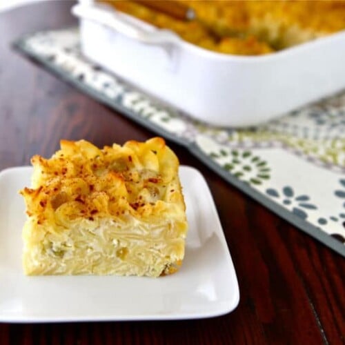 Sweet Lokshen Kugel on white plate, with container in background, on patterned placemat, on wooden table.