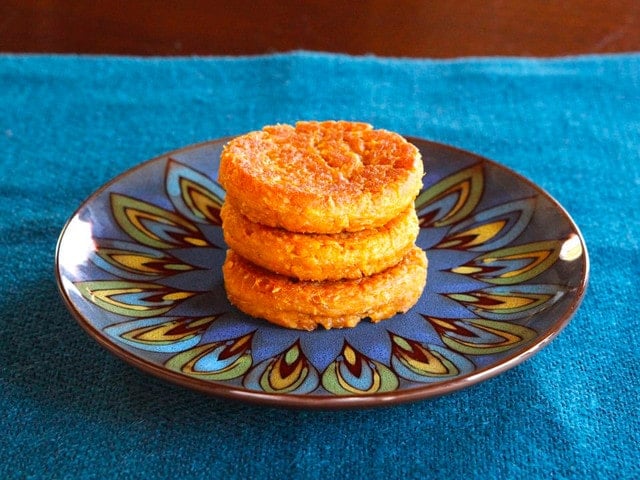 Pile of three sweet potato coconut chremslach - mashed potato latkes on a peacock feather-design plate on a teal placemat. 