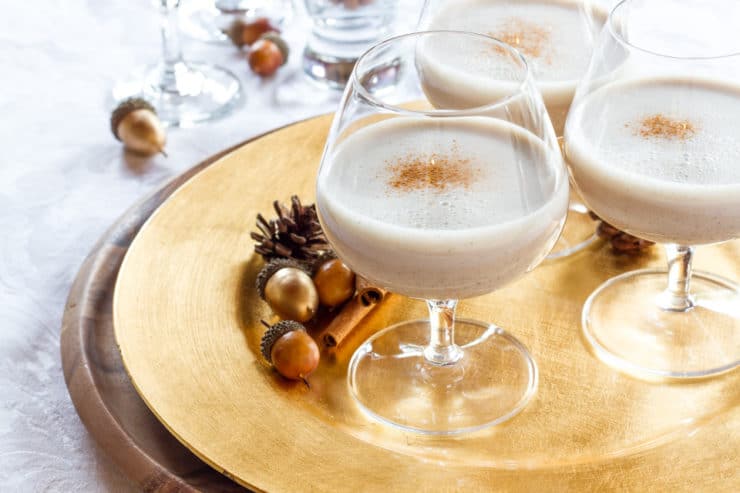 Three glasses of Vegan Eggnog made served on a gold plate with nuts and cinnamon designs