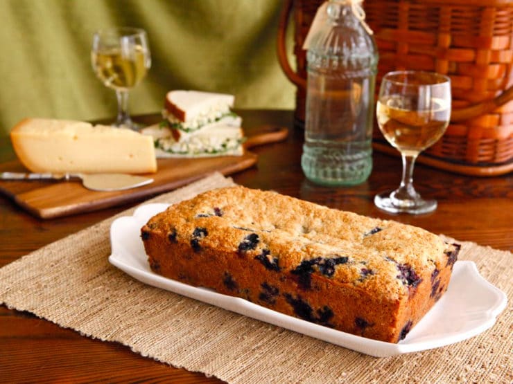 Blueberry Cake served on a white plate with a glass of win and a sliced cheese beside