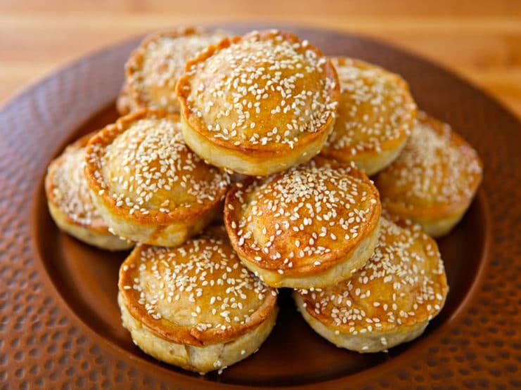 Sephardic Meat Hand Pies sprinkled with sesame seeds stock on top of each other served in a fancy brown plate