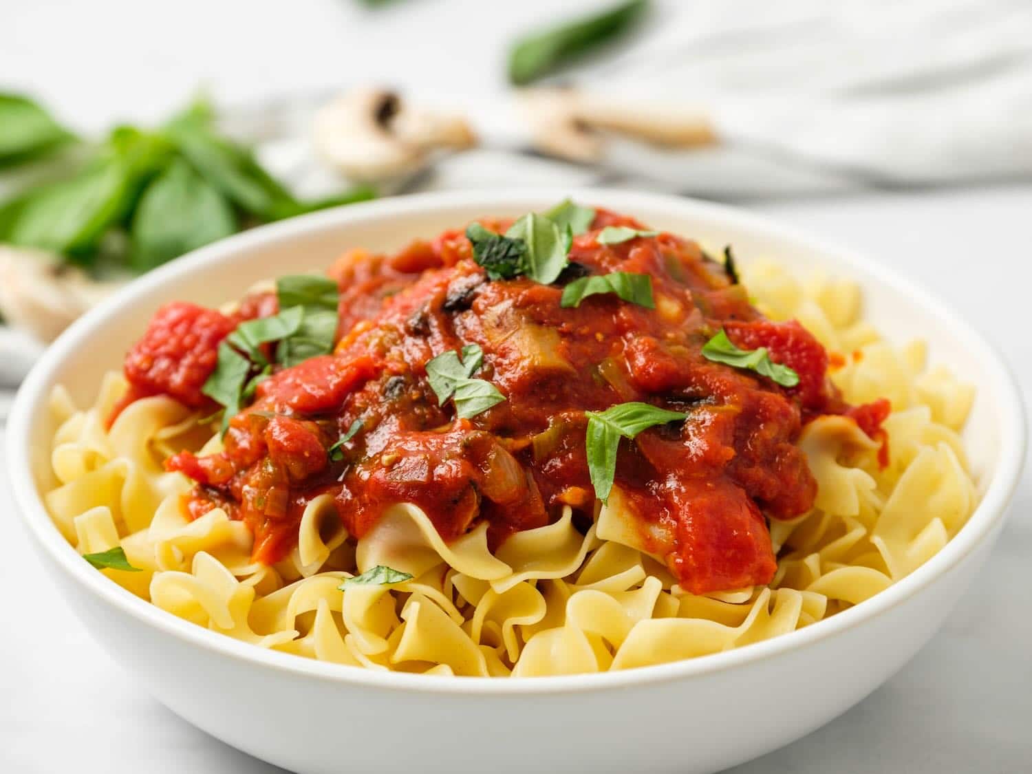 Horizonal shot of a bowl of egg noodles topped with chicken cacciatore in tomato sauce and garnished with parsley.