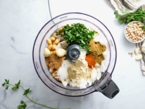 Horizontal overhead image of a food processor bowl filled with falafel ingredients.