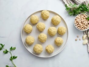 Horizontal overhead image of a white plain containing uncooked falafel balls.