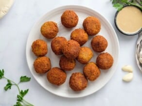 Horizontal overhead image of a white plate filled with falafel balls.